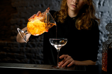 Girl bartender pours ready-made cocktail into glass.