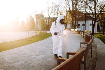 Man wearing protective suit disinfecting public places in the sun with spray chemicals to...