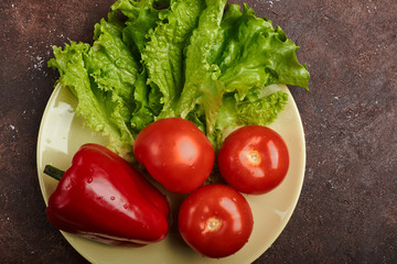 fresh veggies pepper tomatoes and lettuce on a plate on a brown background isolated