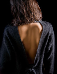 Close-up detail photo of young woman wearing open back blouse on black background