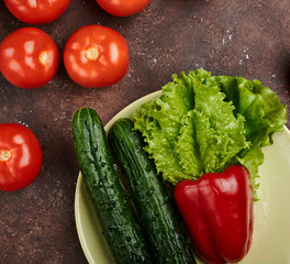 fresh veggies pepper tomatoes cucumbers and lettuce on a plate on a brown background isolated