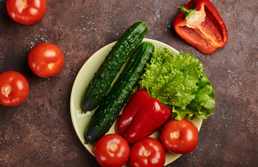 fresh veggies pepper tomatoes cucumbers and lettuce on a plate on a brown background isolated