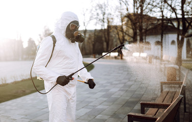Man in virus protective suit and mask disinfects public places  with spray chemicals to prevent the...