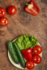 fresh veggies pepper tomatoes cucumbers and lettuce on a plate on a wooden background isolated