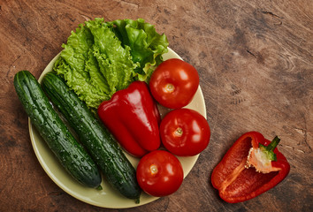 fresh veggies pepper tomatoes cucumbers and lettuce on a plate on a wooden background isolated
