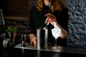 Young bartender mixed cocktail in large mixing cup with bar spoon.