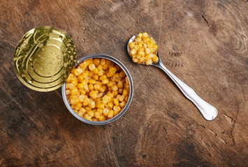 sweet corn grains witn spoon in a tin open can on a wooden background