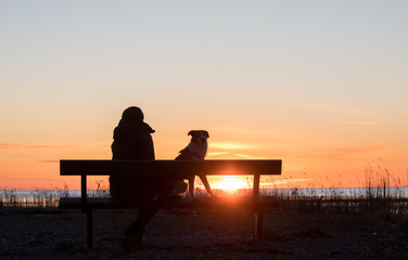 Fototapeta na wymiar Portrait of the women, sitting on the bench, enjoying the seacoast sunset with the dog friend