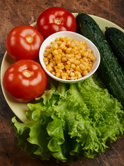 fresh veggies corn tomatoes cucumbers and lettuce on a plate on a wooden background isolated