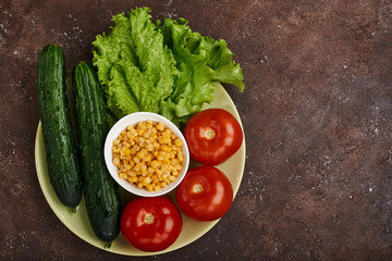 fresh veggies corn tomatoes cucumbers and lettuce on a plate on a brown background isolated