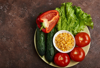 fresh veggies corn tomatoes cucumbers and lettuce on a plate on a brown background isolated