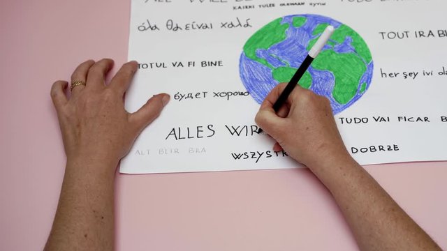 Hands write all will be ok in many languages around a colorful earth. Close up