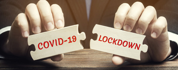 A man collects wooden puzzles with the words Covid-19 and Lockdown. Coronavirus pandemic infection...