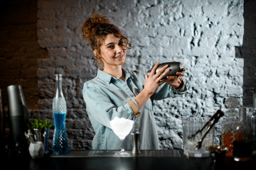 Lady at bar holds shaker in her hands and shake it