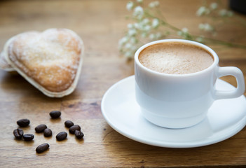 
White cup with latte coffee and fresh pastries on a wooden table