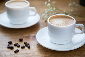 
Two white cups with latte coffee and flowers on a wooden table