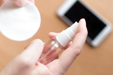 Woman hand holding antiseptic for disinfect screen of mobile phone. Female cleaning with sanitizer gel. Coronavirus or covid-19 prevention. Protection concept.