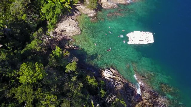 Aerial bird's eye view of Coastline with Yacht docked in tropical private beach with people swimming  - sapphire waters, Playa Mita, Riviera Nayarit, Mexico