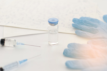 Medicine bottle, blue rubber gloves, syringes, papers with handwritten formulas on light background. Coronavirus vaccine development. 2019-nCoV liquid drug, virus antidote. Copy space. Health concept.