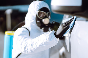 Hand of Man in protective suit washing and disinfection handles of a car, to preventing the spread...