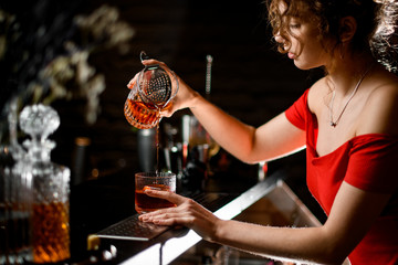 beautiful woman in red blouse pours alcoholic drink into glass at bar.