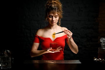 young beautiful girl holds glass with cocktail and tweezers with slice of citrus.