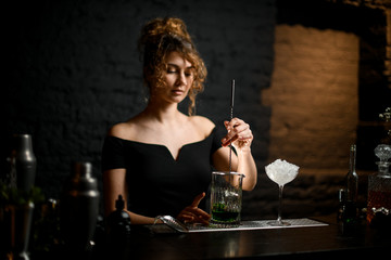Beauty young woman bartender mixed cocktail by long bar spoon.
