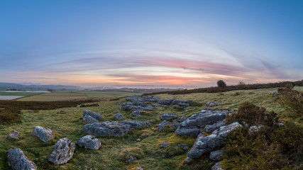 Colourful sunrise over a green valley with a town and mountains in the distance through the morning mist.