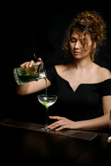 beautiful woman in black blouse pours alcoholic drink into glass at bar.