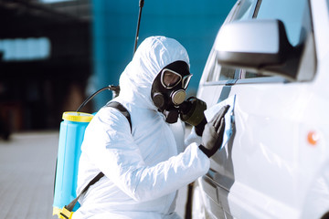 Man in protective suit washing and disinfection handles of a car, to preventing the spread of the...