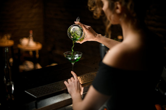 Beauty Woman Bartender In Black Blouse Pours Alcoholic Drink Into Glass At Bar.