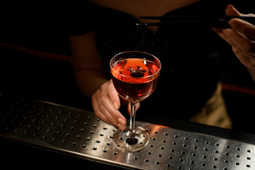 Close-up of glass with cocktail that barman woman decorates with berry