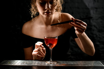 Beautiful young woman at bar decorates glass with alcoholic drink by berry
