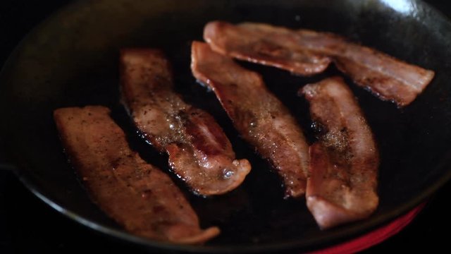Streaky Bacon frying in black cast iron skillet