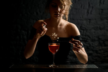 attractive sexy girl at bar decorates glass with alcoholic drink by flowering branch