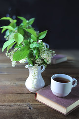 cup of tea or coffee and a branch with flowers. wooden table.