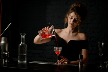 attractive woman bartender in black blouse pours alcoholic drink into glass at bar.