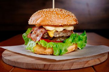 classic burger with juicy beef patty, cheese and bacon on a dark background