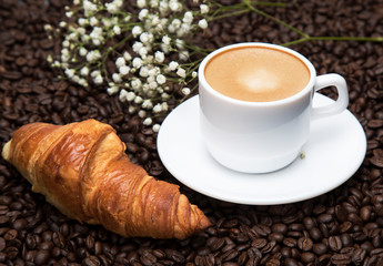 
White cup of coffee latte and croissant on a background of coffee beans