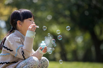 春の公園でシャボン玉を遊んでいる子供