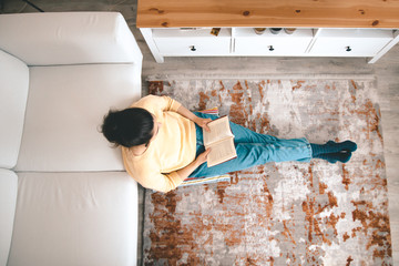 young lady evaluating the quarantine having a good time reading a book by stretching her feet at her home