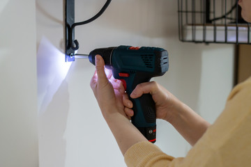 Skilled apprentice young lady repairing the electric socket and the rack with a screwdriver drill at home, due to quarantine