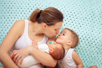 A young woman holds a newborn baby and kisses the eldest son. Mother's love. Mothers Day