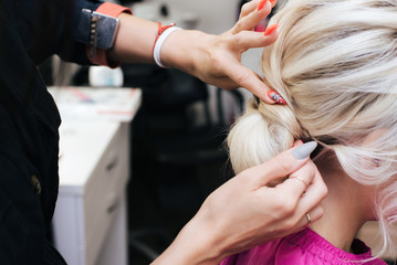 hands of a professional hairdresser make a low bun hairstyle for a blonde girl