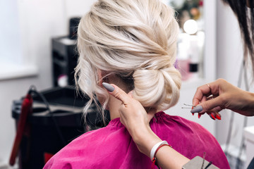 Fototapeta premium hands of a professional hairdresser make a low bun hairstyle for a blonde girl