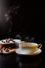 Biscuit with poppy seeds and nuts dusted with icing sugar. From a homemade cake cut a piece. Homemade sponge cake with poppy seeds and nuts, next to it is a cup with tea. Steam rises above the cup.