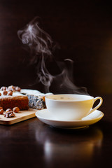 Biscuit with poppy seeds and nuts dusted with icing sugar. From a homemade cake cut a piece. Homemade sponge cake with poppy seeds and nuts, next to it is a cup with tea. Steam rises above the cup.