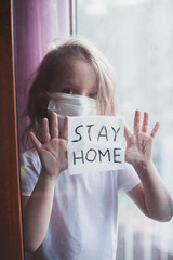 Stay at home quarantine coronavirus pandemic prevention. Sad child both in protective medical masks near windows and looks out window. View from street. Prevention epidemic. Coronavirus concept
