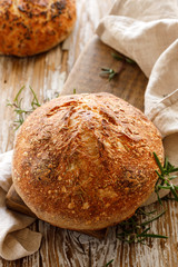 Homemade sourdough loaf of bread with rosemary  on a wooden table, top view