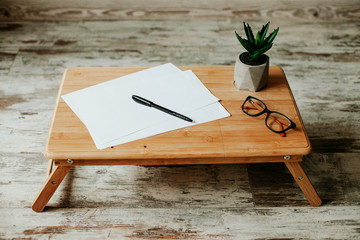 wooden table with blank white paper and pen and glasses and notebook and plant. workplace. business. 